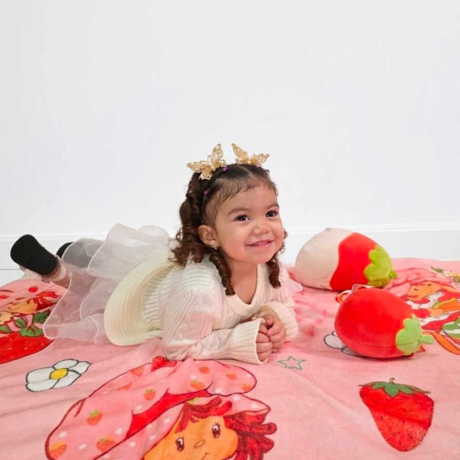 Kler is registered to the contest to win money with this photo: blanket, child, crown, curly_hair, dress, girl, happy, headband, lying_down, pink, playful, plush_toy, portrait, rug, smiling, socks, strawberry, studio, toddler, toy