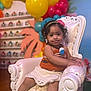 toddler, child, curly_hair, armchair, balloons, party, colorful, playful, cute, indoors, decorations, smiling, sitting, dress, headband, young_child, happy, furniture, celebration, portrait