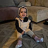 toddler, child, sitting, carpet, living_room, sofa, cushion, knitwear, bonnet, socks, smile, indoors, cozy, floor, furniture, person, cute, young_child, home, comfortable