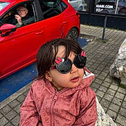 Lina a rejoint le concours — aidez-le/la à gagner de superbes lots ! child, toddler, sunglasses, pink_jacket, rock, sidewalk, red_car, elderly_person, urban, outdoor, curious_expression, winter_clothing, person, vehicle, glasses, pavement, window, hand, street, daylight