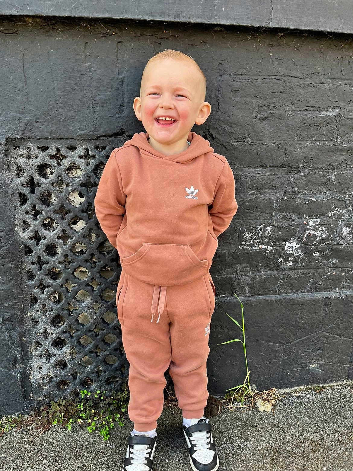 Riley a rejoint le concours — aidez-le/la à gagner de superbes lots ! child, toddler, smiling, happy, outdoor, hoodie, tracksuit, sneakers, standing, concrete, wall, grass, plant, casual_clothing, person, fashion, portrait, young_child, footwear, urban