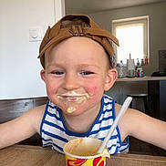 Riley a rejoint le concours — aidez-le/la à gagner de superbes lots ! child, boy, face, cap, hat, ice_cream, food, table, smile, messy, tank_top, striped_clothing, indoor, kitchen, cup, spoon, happy, person, cream, dairy
