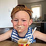child, boy, face, cap, hat, ice_cream, food, table, smile, messy, tank_top, striped_clothing, indoor, kitchen, cup, spoon, happy, person, cream, dairy