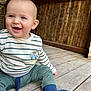 Marius a rejoint le concours — aidez-le/la à gagner de superbes lots ! baby, child, smiling, happy, sitting, striped_shirt, green_pants, blue_socks, wooden_floor, wooden_fence, outdoor, cute, portrait, person, infant, playful, casual_clothing, daylight, expression, young