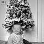 baby, child, christmas_tree, holiday, pajamas, bib, smiling, indoor, floor, decorations, ornaments, pine, star, sitting, tiled_floor, person, festive, monochrome, cute, young_child