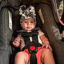 baby, child, car_seat, headband, straps, infant, cute, clothing, sitting, indoor, looking, pout, safety_harness, person, young_child, shorts, white_shirt, accessory, seat, secure