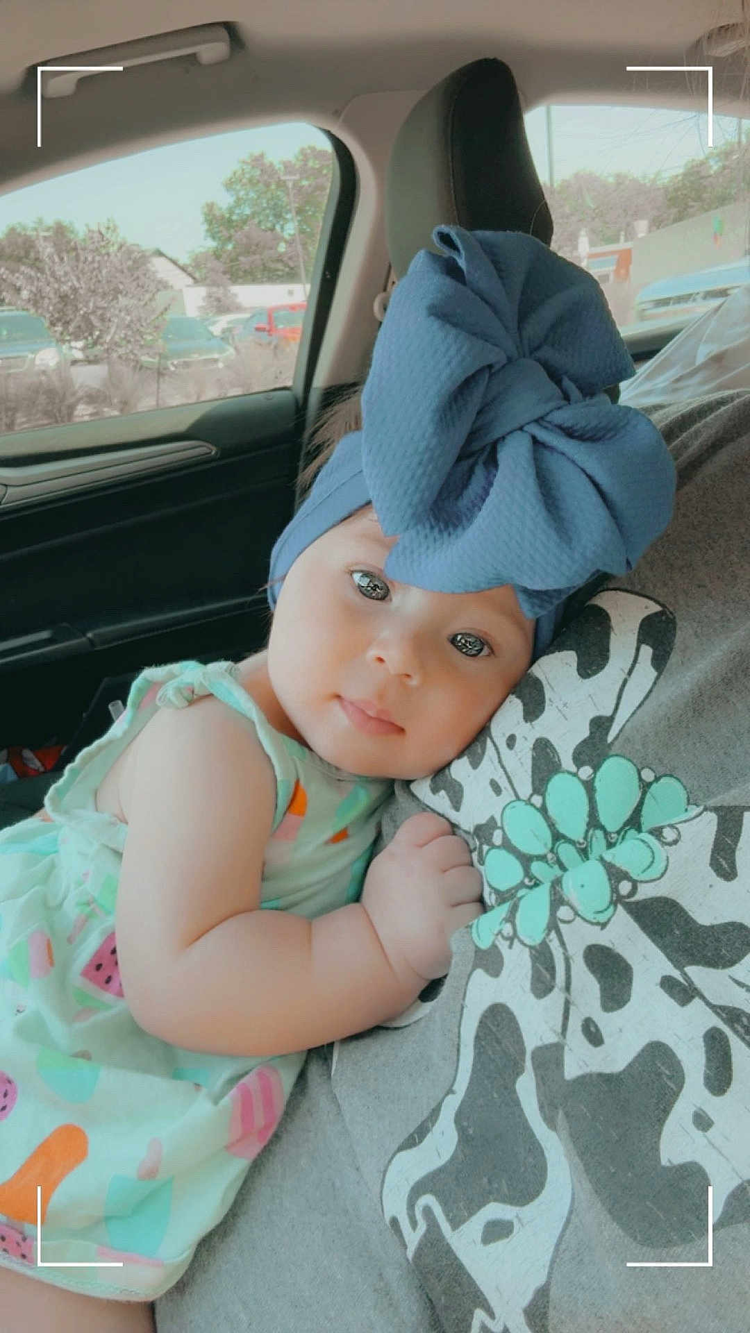 Lainey is registered to the contest to win money with this photo: baby, child, blue_bow, headband, car_interior, person, dress, cute, snuggling, portrait, window, seat, hand, face, clothing, pattern, flower_design, daylight, skin, young_child