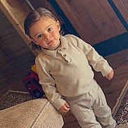Aaron participe au concours pour gagner de l'argent avec cette photo : toddler, child, indoor, wooden_cabinet, toy_truck, couch, rug, floor, clothing, boots, curly_hair, face, standing, home, furniture, expression, cozy, beige, person, portrait