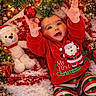 baby, child, christmas_tree, christmas_ornament, holiday_lights, teddy_bear, snow, festive_clothing, red_hoodie, striped_pants, gift_boxes, candy_cane, holiday_decor, smiling, reaching_hands, indoors, celebration, happy, seasonal, festive