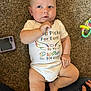 baby, infant, carpet, onesie, clothing, person, child, toy, phone_case, hand, legs, feet, sitting, curious, indoor, cute, skin, head, blue_eyes, casual