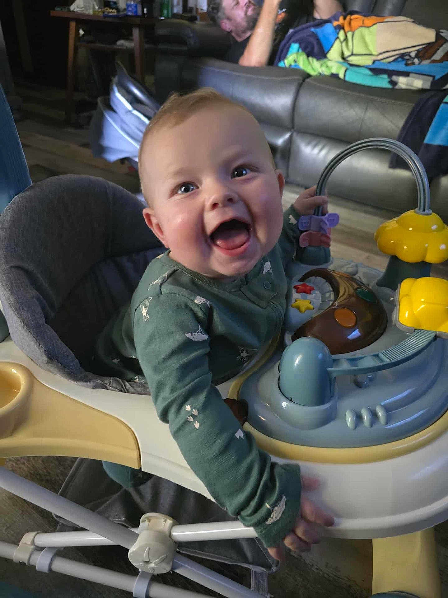 Nico joined the competition — help win amazing prizes! baby, baby_walker, smiling, toy, indoor, person, man, couch, furniture, clothing, happy, child, play, floor, home, relaxing, colorful, seat, joy, infant