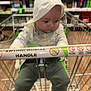 baby, blur, child, clothing, floor, handle, hood, indoors, infant, metal, pants, person, product, retail, shelf, shopping_cart, sitting, socks, store, supermarket