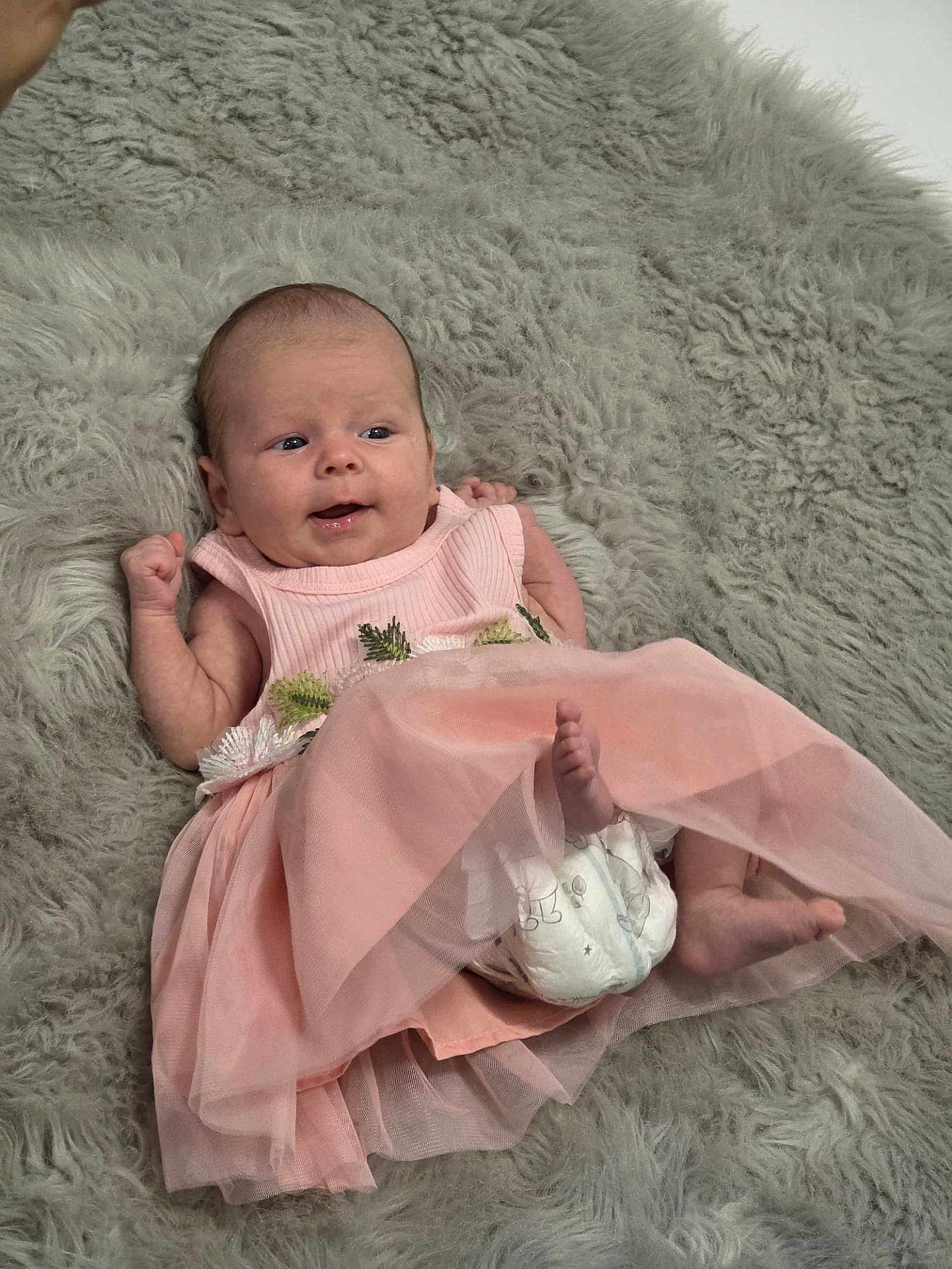 Astrid is registered to the contest to win money with this photo: baby, infant, pink_dress, diaper, fluffy_rug, smiling, lying_down, cute, child, soft_texture, indoors, skin, head, face, barefoot, newborn, happy, small, clothing, playful