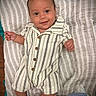 baby, child, smile, romper, sandals, striped_clothing, blanket, lying_down, happy, portrait, infant, cute, face, person, indoors, comfortable, young_child, skin, head, hands