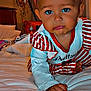 baby, child, bed, red_bow, striped_clothing, crawling, indoor, lamp, pillow, blanket, headband, cute, infant, person, face, hand, foot, expression, room, furniture