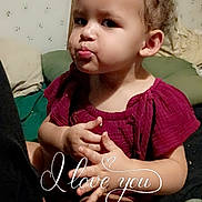 Theresa is registered to the contest to win money with this photo: toddler, child, curly_hair, red_dress, indoor, hands, expression, pillow, wallpaper, sitting, cute, face, portrait, person, baby, cozy, text_overlay, love, affection, casual