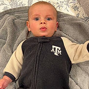 Stetson is registered to the contest to win money with this photo: baby, infant, child, face, eyes, blanket, clothing, black, cream, logo, texas_a&m, indoor, portrait, cute, lying_down, soft_texture, hand, expression, young, person