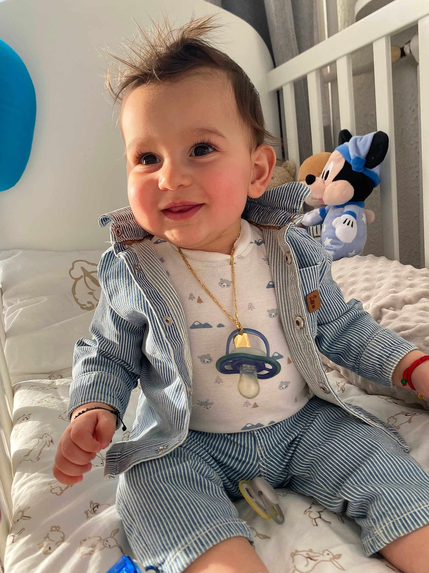 Antonio participe au concours pour gagner de l'argent avec cette photo : child, baby, infant, toddler, smiling, sitting, crib, nursery, pacifier, pacifier_necklace, plush_toy, mickey_mouse, striped_clothing, denim_jacket, gold_chain, rosy_cheeks, long_eyelashes, bed_sheet, blanket, happy