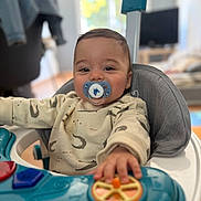 Livio a rejoint le concours — aidez-le/la à gagner de superbes lots ! baby, pacifier, high_chair, toy, indoor, child, smiling, clothing, face, hand, person, furniture, blurred_background, home, play, young_child, infant, cute, sitting, expression