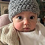 baby, child, knit_hat, pom_pom, beige_sweater, indoor, face, wide_eyes, curious, infant, portrait, cute, warm_clothing, soft_lighting, background, fireplace, framed_picture, cozy, close_up, person