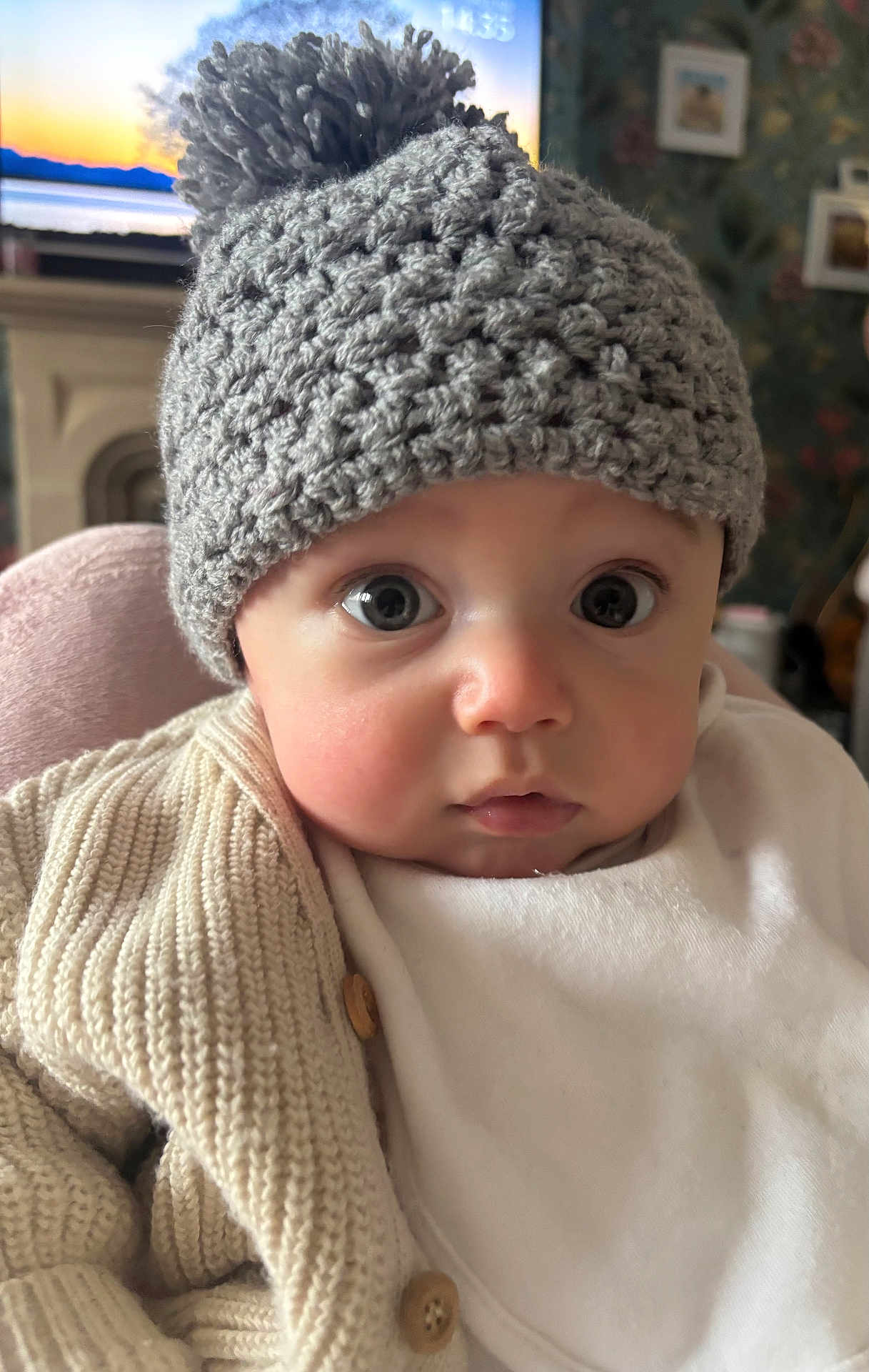 Dougie joined the competition — help win amazing prizes! baby, child, knit_hat, pom_pom, beige_sweater, indoor, face, wide_eyes, curious, infant, portrait, cute, warm_clothing, soft_lighting, background, fireplace, framed_picture, cozy, close_up, person