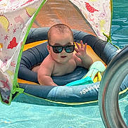 Zion is registered to the contest to win money with this photo: baby, canopy, child, cute, dinosaur_pattern, float, fun, infant, leisure, outdoor, pool, relaxing, summer, sunglasses, sunlight, swimming, toy, vacation, water, waving