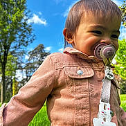 Owena a rejoint le concours — aidez-le/la à gagner de superbes lots ! toddler, child, pacifier, pink_jacket, outdoor, park, grass, trees, sky, clouds, nature, cute, portrait, happy, baby, clothing, daylight, young_child, smile, person