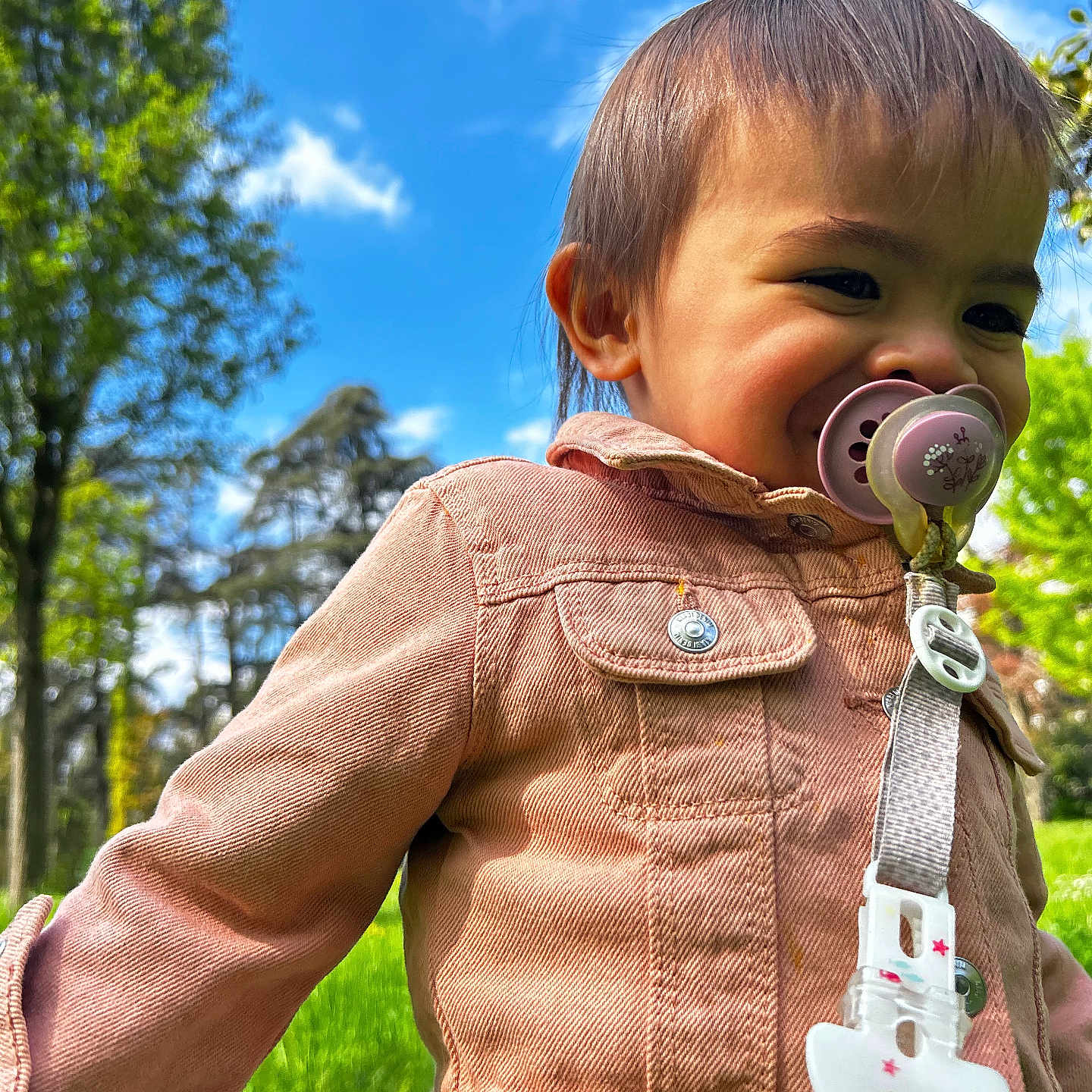 Owena a rejoint le concours — aidez-le/la à gagner de superbes lots ! toddler, child, pacifier, pink_jacket, outdoor, park, grass, trees, sky, clouds, nature, cute, portrait, happy, baby, clothing, daylight, young_child, smile, person