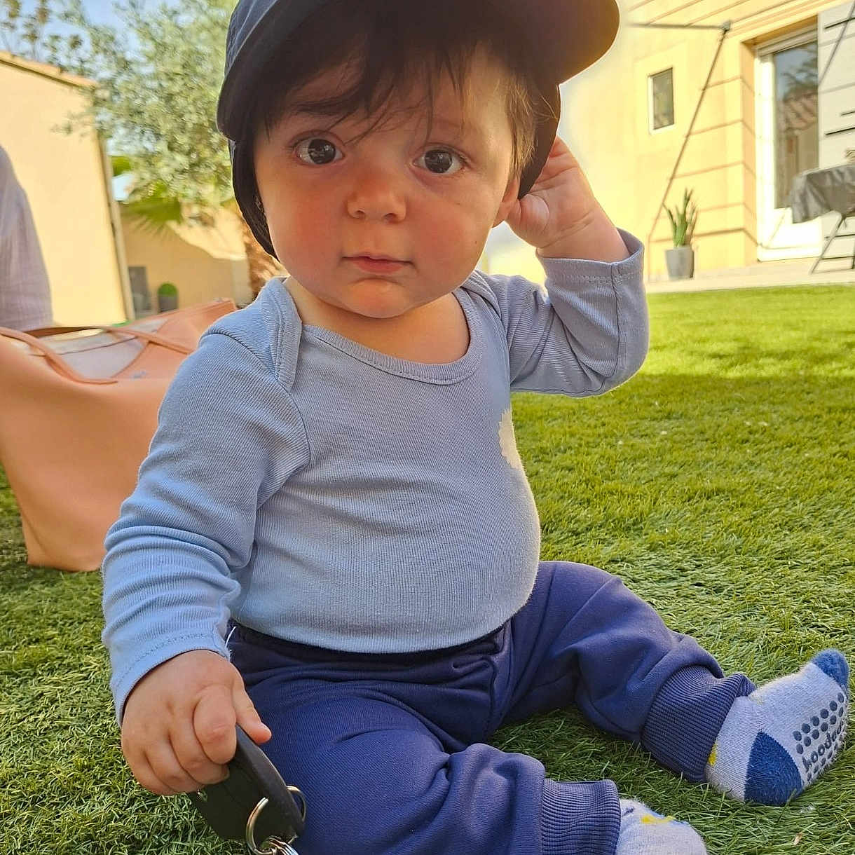 Tiago a rejoint le concours — aidez-le/la à gagner de superbes lots ! child, toddler, baby, grass, cap, keys, outdoor, sunlight, blue_clothing, socks, person, greenery, curious, sitting, toy, hand, face, young, casual, daylight