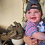 Grayson joined the competition — help win amazing prizes! baby, child, smiling, cap, blue_eyes, striped_shirt, diaper, adult_hand, ring, stone_frog, plant, flower_pot, indoor, person, holding, happy, cute, portrait, casual, home