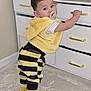 Liam is registered to the contest to win money with this photo: baby, toddler, pacifier, standing, dresser, drawers, toy_car, yellow_clothing, striped_pants, socks, hooded_vest, carpet, gold_handle, nursery, looking_at_camera, curious, indoor, plush_fabric, short_hair, person