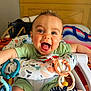 baby, child, smiling, happy, indoor, toys, baby_seat, colorful, clothing, headboard, blanket, face, person, playful, teething_toys, green_outfit, infant, cute, joyful, closeup