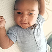 Taïlane a rejoint le concours — aidez-le/la à gagner de superbes lots ! baby, infant, child, person, face, skin, blue_clothing, onesie, buttoned_clothing, lying_down, raised_arm, soft_surface, white_background, cute, portrait, closeup, young, expression, indoors, newborn