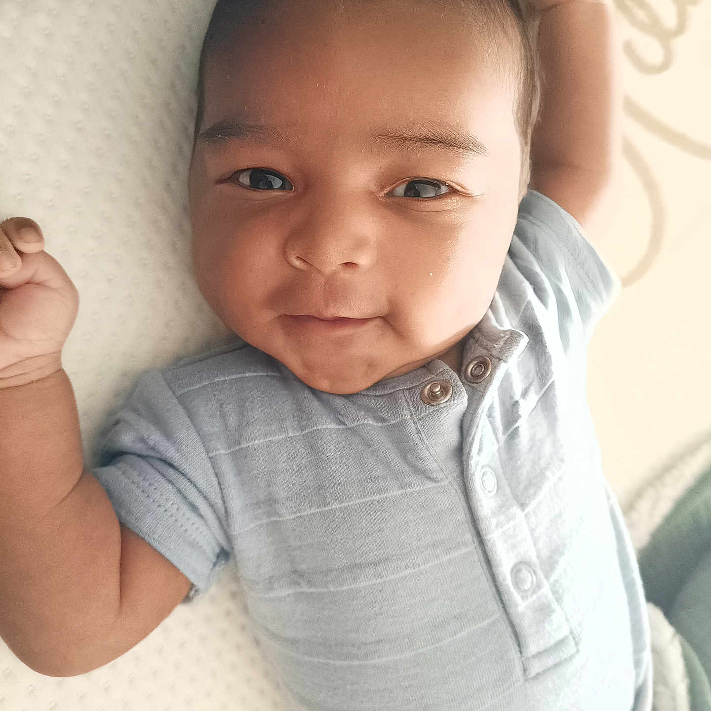 Taïlane a rejoint le concours — aidez-le/la à gagner de superbes lots ! baby, blue_clothing, buttoned_clothing, child, closeup, cute, expression, face, indoors, infant, lying_down, newborn, onesie, person, portrait, raised_arm, skin, soft_surface, white_background, young