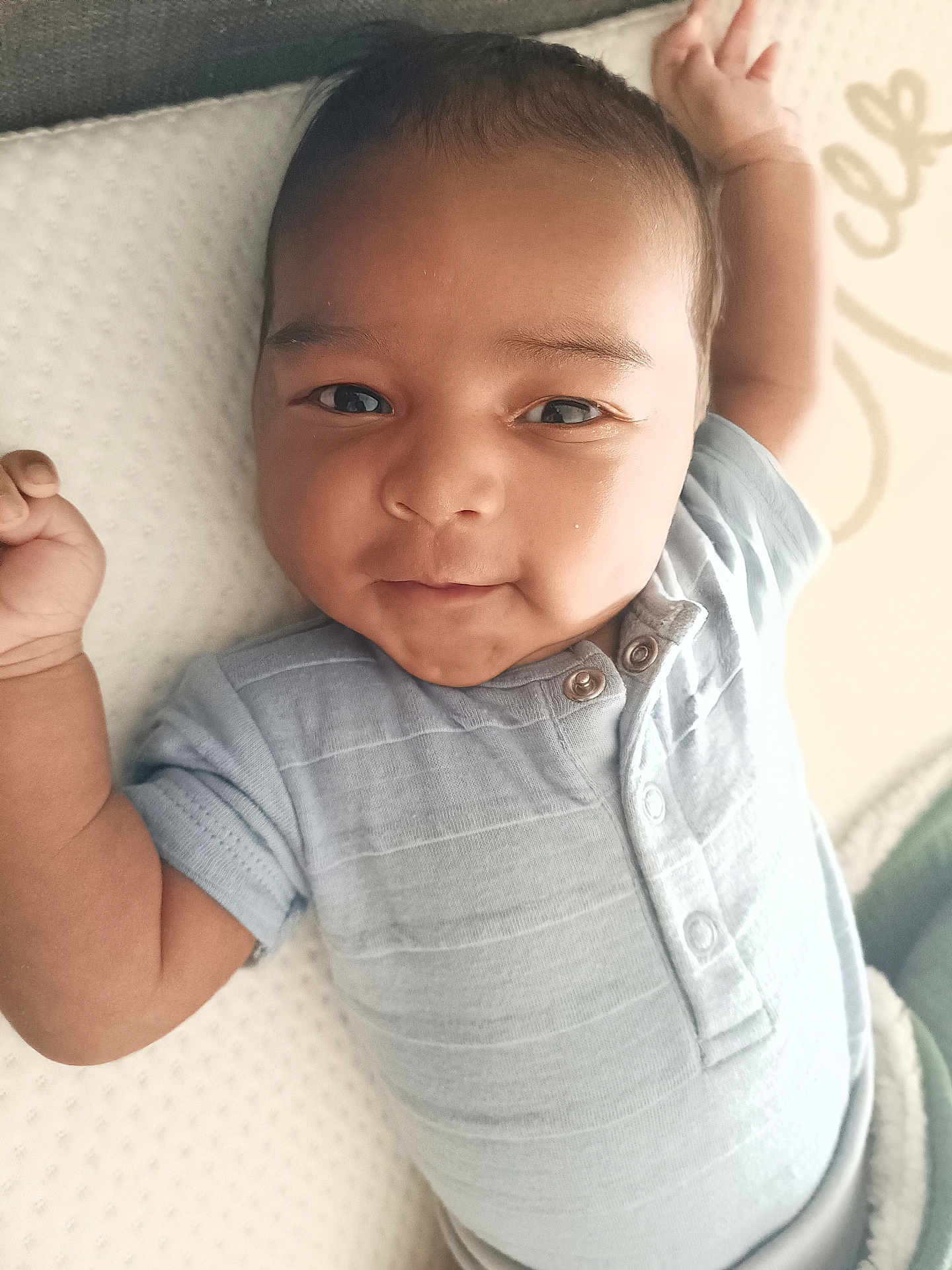 Taïlane a rejoint le concours — aidez-le/la à gagner de superbes lots ! baby, infant, child, person, face, skin, blue_clothing, onesie, buttoned_clothing, lying_down, raised_arm, soft_surface, white_background, cute, portrait, closeup, young, expression, indoors, newborn