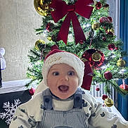 Tymaë a rejoint le concours — aidez-le/la à gagner de superbes lots ! baby, celebration, child, christmas_tree, cute, decorations, face, festive, happy, high_chair, holiday, indoor, ornaments, overalls, person, red_bow, santa_hat, seasonal, smiling, sweater