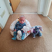 Max is registered to the contest to win money with this photo: baby, infant, child, pajamas, inflatable_chair, plush_toy, elephant_toy, carpet, indoor, door, hallway, home, person, seated, cute, toy, floor, soft, comfortable, curious