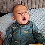 baby, infant, onesie, blue_clothing, dog_pattern, blanket, soft_texture, plush_toy, yawning, curious_expression, indoor, child, person, cute, lying_down, head, face, sleepwear, comfort, cozy