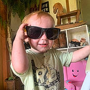 Wesley joined the competition — help win amazing prizes! boots, child, cute, dinosaur_tshirt, dirt, door, face, floor, hand, home, indoor, pink_chair, plant, shelf, short_sleeve_shirt, smiling, sunglasses, toddler, toy, wooden_rocking_horse