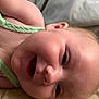 baby, infant, face, smile, skin, clothing, green, lying_down, closeup, child, head, cheek, eye, nose, mouth, ear, fabric, bed, pillow, soft
