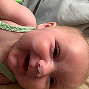 Wisteria joined the competition — help win amazing prizes! baby, smile, face, infant, skin, cheeks, green_clothing, lying_down, closeup, head, person, sleeping_area, blanket, soft_surface, happy, cute, young_child, indoors, portrait, warm