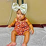 baby, child, headband, bow, romper, floral, sitting, barefoot, medical_table, paper_cover, curious, indoors, skin, legs, arms, cute, expression, infant, person, portrait