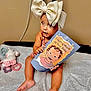 Malaysia joined the competition — help win amazing prizes! baby, child, bow, headwear, pamphlet, booklet, toy, stuffed_animal, bed, sheet, sitting, indoor, curious, holding, skin, person, foot, hand, eyes, clothing