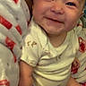 baby, infant, child, smiling, happy, portrait, sitting, blanket, bed, indoors, face, eyes, clothing, onesie, patterned_blanket, cozy, close_up, front_view, baby_photo, family_snapshot