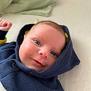 Gabriel a rejoint le concours — aidez-le/la à gagner de superbes lots ! baby, infant, face, smile, hoodie, blue_clothing, lying_down, pillow, closeup, skin, eyes, cheeks, newborn, child, cute, expression, indoors, fabric, soft, portrait