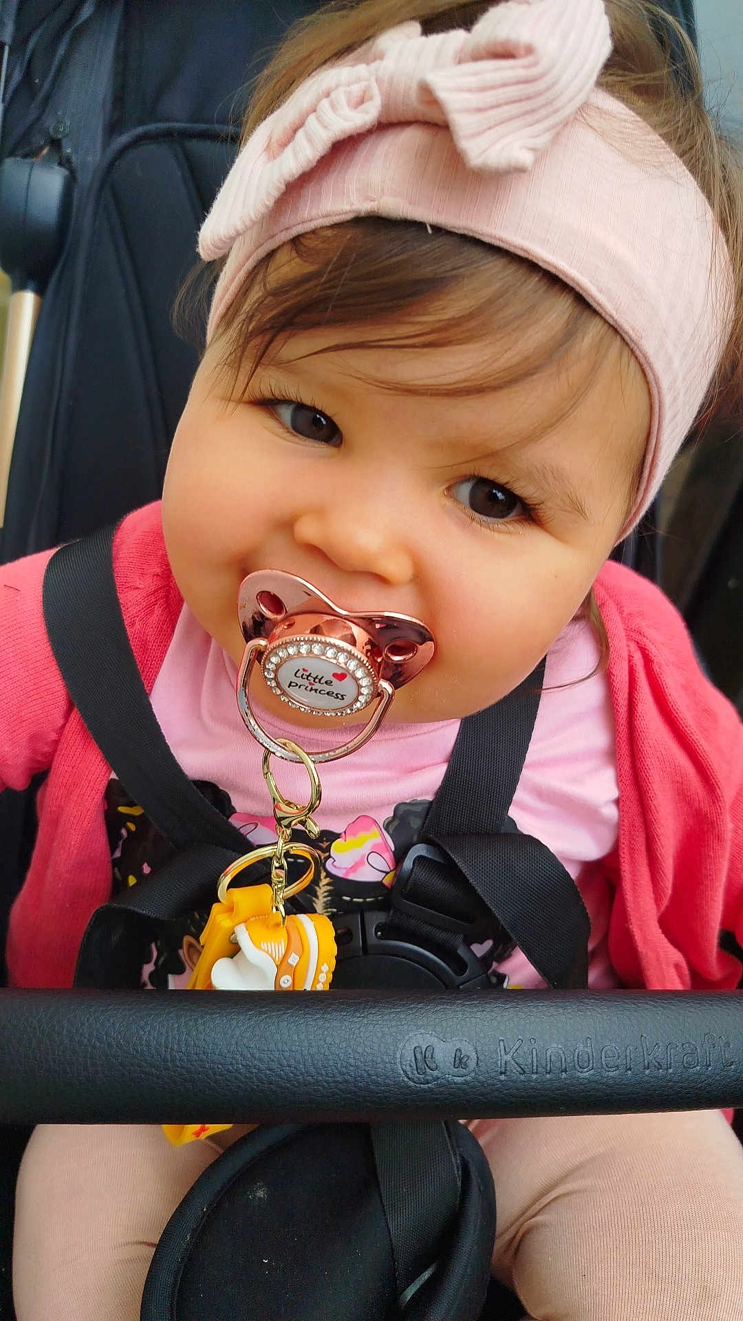 Zheïna participe au concours pour gagner de l'argent avec cette photo : toddler, child, pacifier, headband, pink_clothing, stroller, toy, smiling, face, baby, closeup, seatbelt, cute, infant, person, outdoor, happy, young_child, accessory, portrait