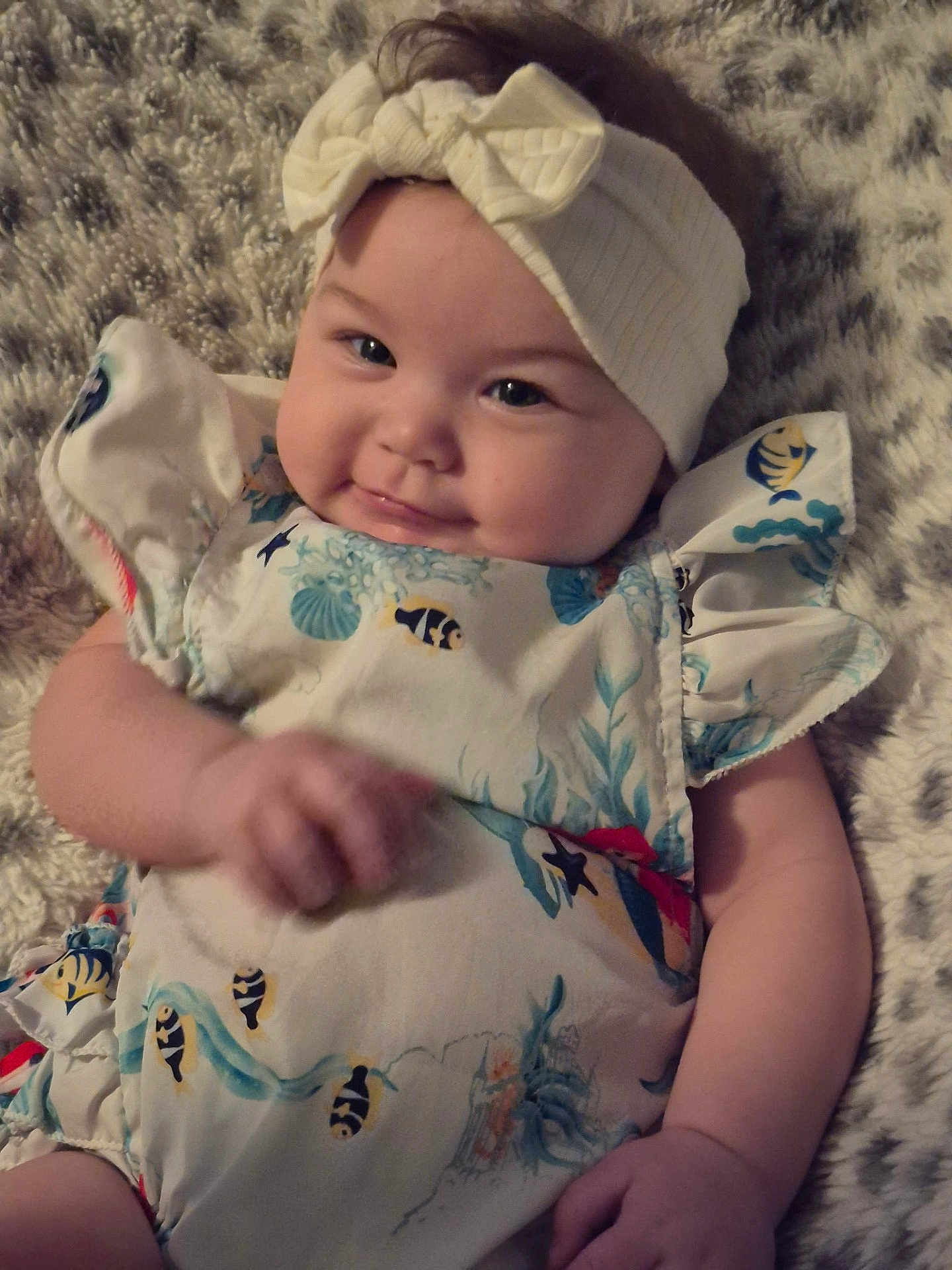 Lucrezia joined the competition — help win amazing prizes! baby, infant, headband, bow, dress, fish_pattern, smile, hand, fluffy_blanket, lying_down, cute, chubby_cheeks, person, child, apparel, fabric, pattern, skin, face, young