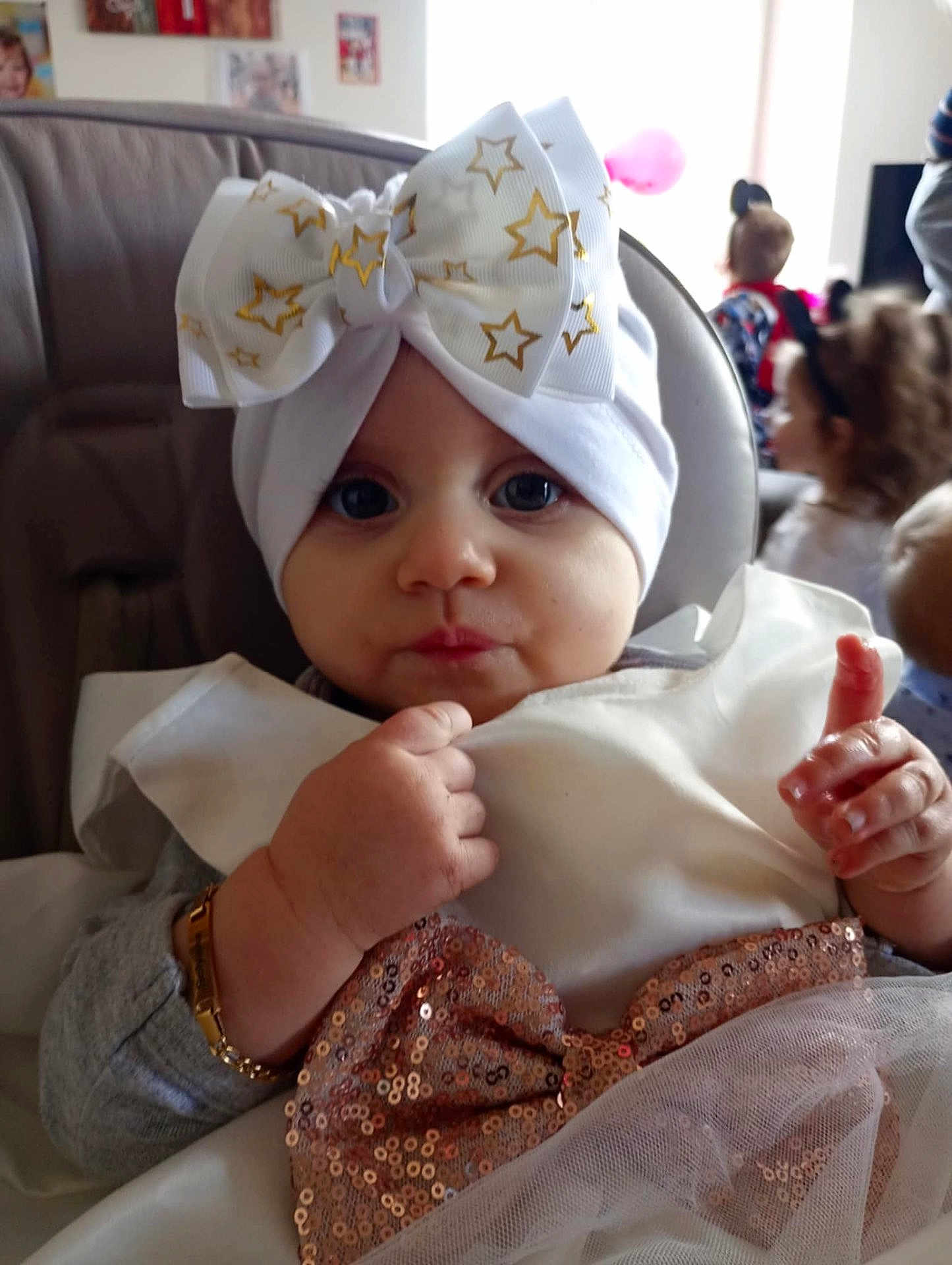 Solyana participe au concours pour gagner de l'argent avec cette photo : baby, infant, toddler, bow, headwrap, blue_eyes, portrait, close_up, bracelet, sequin_dress, white_clothing, highchair, hand, face, cheeks, party, balloon, background_children, adorable, cute