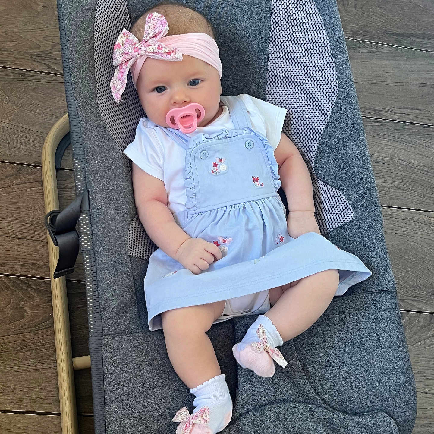 Adriana joined the competition — help win amazing prizes! baby, baby_rocker, blue_dress, bow, child, clothing, comfort, cute, dress, gray_rocker, headband, indoor, infant, pacifier, person, pink_socks, portrait, relaxing, socks, wooden_floor