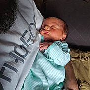 Anthony Allen Pucci joined the competition — help win amazing prizes! baby, newborn, sleeping, infant, adult_arm, pajamas, striped_clothing, person, closeup, indoor, resting, beard, bracelet, hand, gray_shirt, fabric, couch, comfort, portrait, cozy